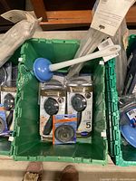 Photo of bin showing blue sink plunger, four packaged showerheads, and packaged drain strainer.