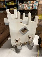 Photo of a white wooden birdhouse with two metal feeders hanging from chains on the front, oval-shaped entry holes, diamond-shaped cut-out above the feeders, and a crown-shaped top edge.