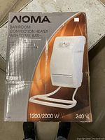 Photo of the Noma bathroom convection heater in its original box showing branding, specifications, and image of the heater with towel bar.