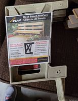 Two grey molded PEAK deck bench brackets lying flat with original packaging showing product details.