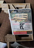 Three beige Peak deck bench brackets with product packaging showing usage instructions and branding.