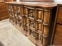 Large wooden dresser with detailed carved front design and metal handles on drawers, shown from front angle.