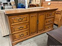 Front view of the wooden dresser showing six drawers and two cupboard doors with brass-style handles, medium brown finish with wood grain texture.