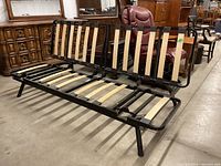 Photo of black metal futon frame showing wooden slats and foldable design in a warehouse setting.