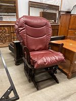 Glider rocker chair with burgundy cushioned seat and backrest, wooden frame and gliding base, photographed from the side angle showing the chair surrounded by other furniture.