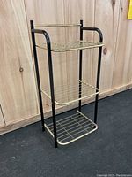 Front view of a metal shelving unit featuring a black frame and three gold wire mesh shelves
