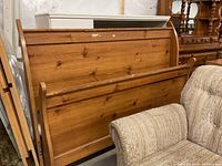 Queen size wooden bed frame parts including headboard, footboard, and rails shown leaning against other furniture, natural wood finish with some wear and dirt.