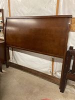 Wooden queen size headboard against wall, showing surface finish and mounting frame beams below and side posts.