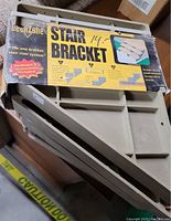 Photo shows two packs of Deck Zone stair brackets, each pack containing two brackets with yellow labeling and installation instructions visible.