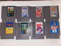 Six Nintendo NES game cartridges laid out flat, showing labels of Golf, Top Gun, Baseball, Volleyball, Tennis, and Ice Hockey games.