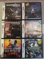 Photo showing front covers of six Nintendo DS games in the lot laid flat: Transformers Autobots, Transformers Decepticons, Star Trek Tactical Assault, Spider-Man Friend or Foe, Justice League Heroes, TMNT.