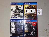 Front view of four PS4 game cases: Ghost of Tsushima, DOOM, The Last of Us Part II, and The Last of Us Remastered (PlayStation Hits).