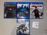 Four PS4 game cases arranged with cover art visible: Injustice 2, Need for Speed, NBA 2K19, Destiny 2.