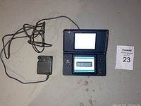 Red Nintendo DS Lite open and powered on with charger placed next to it, screen showing Brain Age game text.