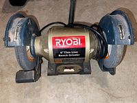 Front view of Ryobi 6-inch thin line bench grinder showing the central motor with Ryobi label and both grinding wheels with guards.