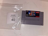 Front of SNES cartridge showing 'The Magical Quest starring Mickey Mouse' game label and auction lot bag with tag.