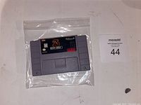 Front view of Mortal Kombat 3 SNES game cartridge sealed in plastic bag with labeled lot number card.