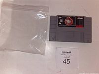 Front of NBA Jam SNES cartridge with label showing title and branding, alongside a clear plastic resealable bag and auction lot number.