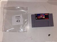 Front side of SNES Aladdin game cartridge along with auction bag with lot number 43.