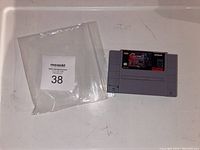 Front view of Contra 3 SNES game cartridge with visible label and auction bag alongside.