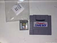 Photo of Super Game Boy and Kirby's Dream Land game cartridges on flat white surface with MaxSold tag.