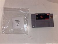 Front view of the SNES The Terminator game cartridge laid flat next to a plastic bag.