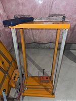 Triton work centre metal frame in orange and silver colors, standing with a blue box on top, showing the main structure and base