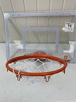 Front view of a mini indoor basketball hoop with clear backboard, orange rim, and white net on a table with wall background.