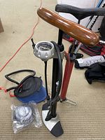 Photo showing two air pumps standing upright on a carpet, one with wooden handle and pressure gauge, the other blue colored foot pump, plus a plastic wrapped spool of tubing.