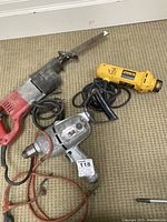 Three power tools on carpet: Milwaukee Sawzall reciprocating saw with blade, Dewalt cut out tool, and Black and Decker hammer drill
