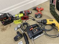 Assorted power tools arranged on carpeted floor showing Black & Decker jigsaw, DeWalt corded drill, several cordless drills, batteries and battery charger.