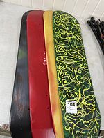 Photo of four skateboard decks stacked with top deck showing yellow and green scribble design, middle decks red and black with visible wear, and bottom deck yellow wood