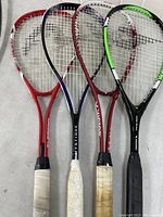 Four assorted squash racquets displayed side by side showing name brands and worn grips.