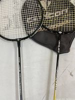 Two badminton racquets shown on a white surface, one with Black Knight BK-150 branding, accompanied by a Carlton cover.