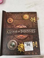 Front cover of the Game of Thrones pop-up book with intricate embossed design and sigils, showing label and tear damage on the top left.