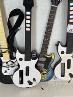 Three Guitar Hero guitar controllers arranged side by side on a surface, featuring distinct designs and cable attachments.