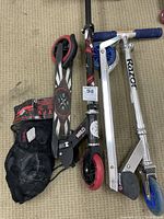 Photo showing two folding kick scooters (Razor and WRLD Industries) and a black mesh bag with youth protective gear.