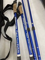 Two blue Alpine Keen Fit walking sticks showing cork handles and printed text along shafts, lying on a table alongside a carrying case strap.