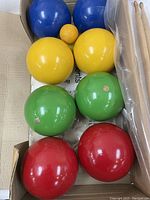 All bocci balls and sticks arranged in a box showing the set contents including eight colorful wooden balls, two smaller yellow balls, and two wooden sticks.