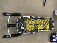 Full overview of the Ski-Doo custom toboggan sled showing the yellow perforated nylon decking with black Ski-Doo logo, aluminum frame, front ski runners, and ski handles.