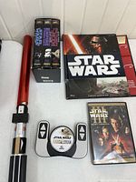 Photo showing the Star Wars Light Saber BBQ Tongs, the original trilogy VHS set, the Star Wars Episode III DVD, the Mandalorian Jam'n controller, and the Star Wars Flashlight Adventure Book.