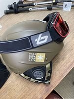 Side view of matte olive green Urge ski helmet with Bolle ski goggles attached showing the strap and helmet vents.