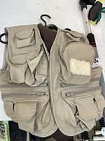 Beige vintage fly fishing vest with multiple pockets and fleece patch on chest pocket.