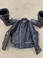 Full view of black leather motorcycle jacket laid flat with two black motocross boots on either side.