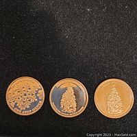 Three copper coins placed side by side showing Christmas tree and snowflake designs on one side