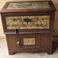 Full view of antique wooden box with decorative panels, hinged lid on top, and two front doors below.