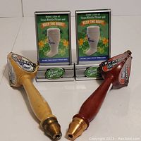 Photo showing two Rickards beer tap handles in natural and reddish wood with brass ends and detailed branding logos, arranged side-by-side.