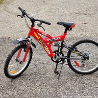 Side angle showing red CCM Menace Tech Team boys bike with front and rear suspension, 20-inch tires, and 6-speed gear system.