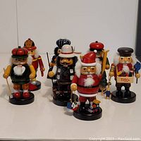Front and side view of seven wooden Christmas nutcracker statues displaying different characters, all standing upright on a flat surface.