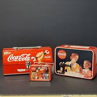 Three Coca-Cola branded items: mini toolbox, tin can, and a hanging ornament (detail of ornament not clear)